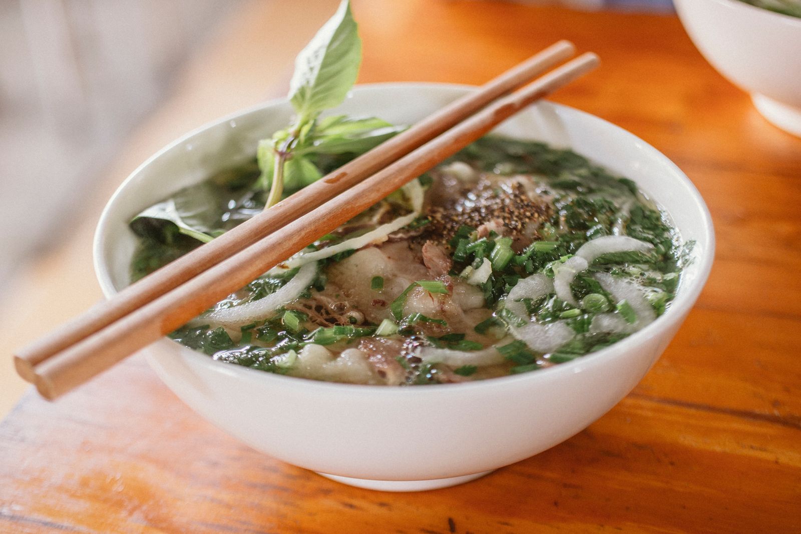 Bowl of beef pho with basil and chopsticks
