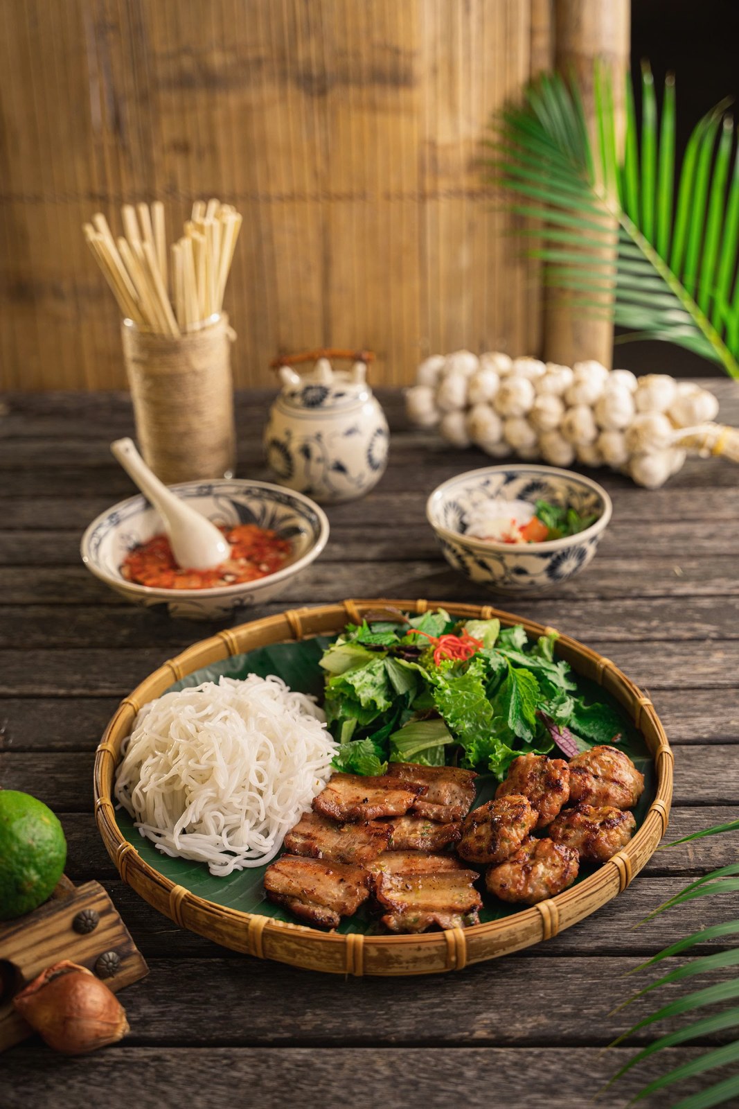 Grilled pork with rice noodles, fresh herbs and dipping sauces on a wooden table
